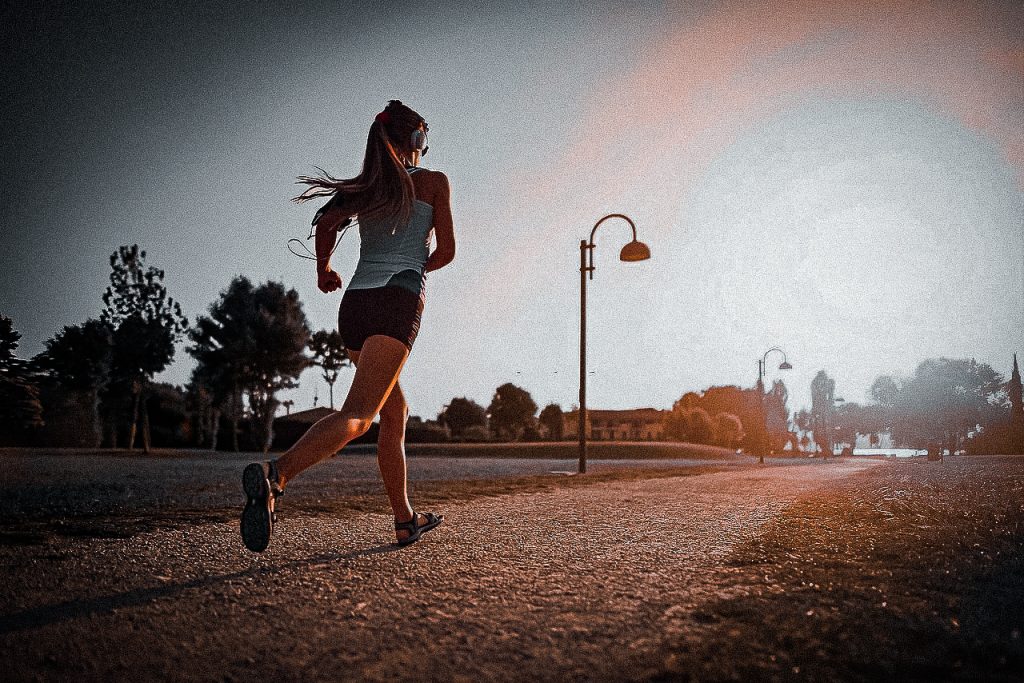 Woman jogging next to a road at sunset.