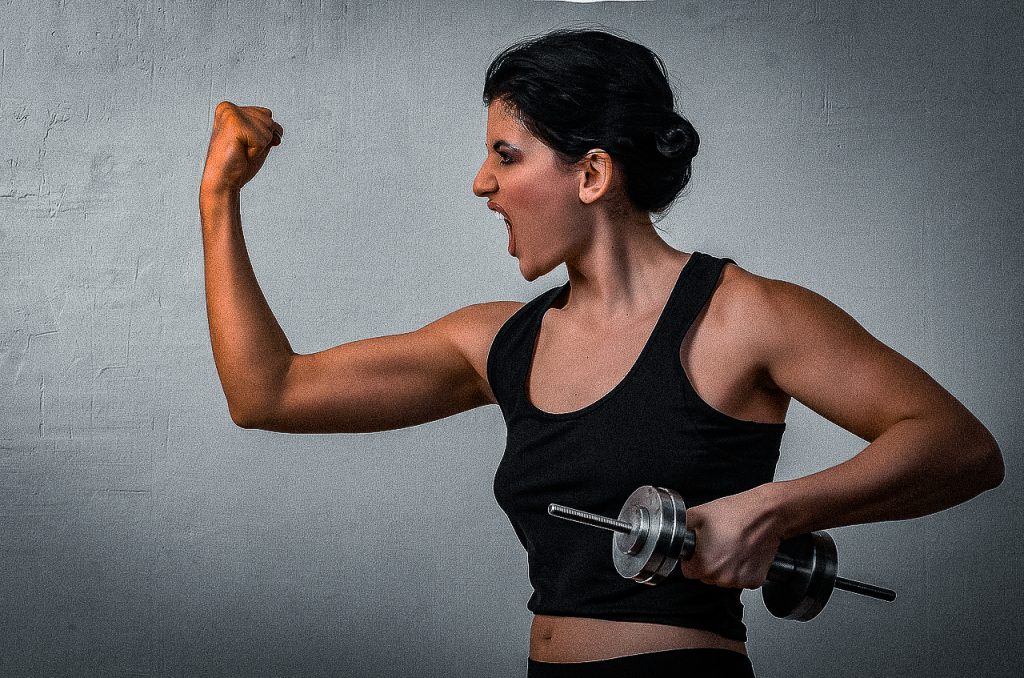 Woman flexes her muscles and yells emphatically. 